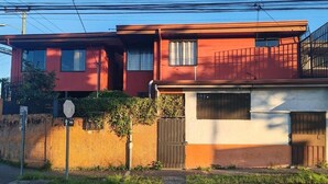 A two-story residential building with a red and white facade, a gated entrance, and a visible street sign. - Centrally located and furnished apartment for short stays (San José)