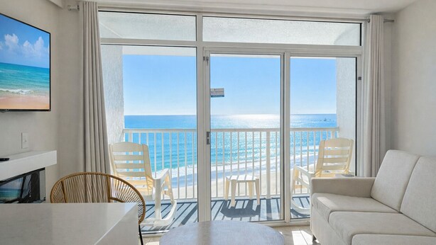 A room with a balcony overlooking the ocean, furnished with a sofa, chairs, and a table.
