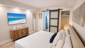 A bedroom with a bed, a wooden dresser, a TV, and a sliding door leading to a bathroom.
