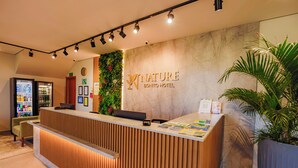 Ein Hotelrezeptionstresen mit Holzoptik, eine Wandpflanze und ein Schild mit der Aufschrift 'NATURE BONITO HOTEL'.