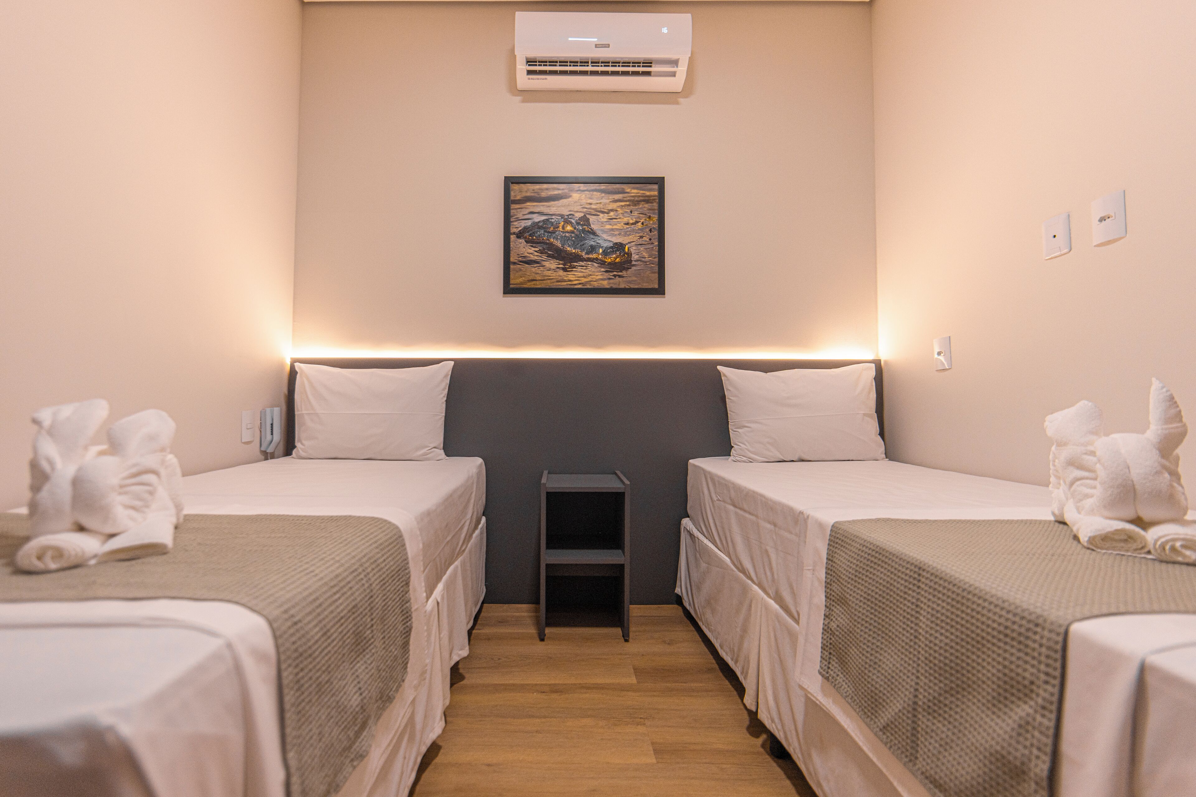 Habitación de hotel con dos camas individuales, una mesita, aire acondicionado y un cuadro en la pared.