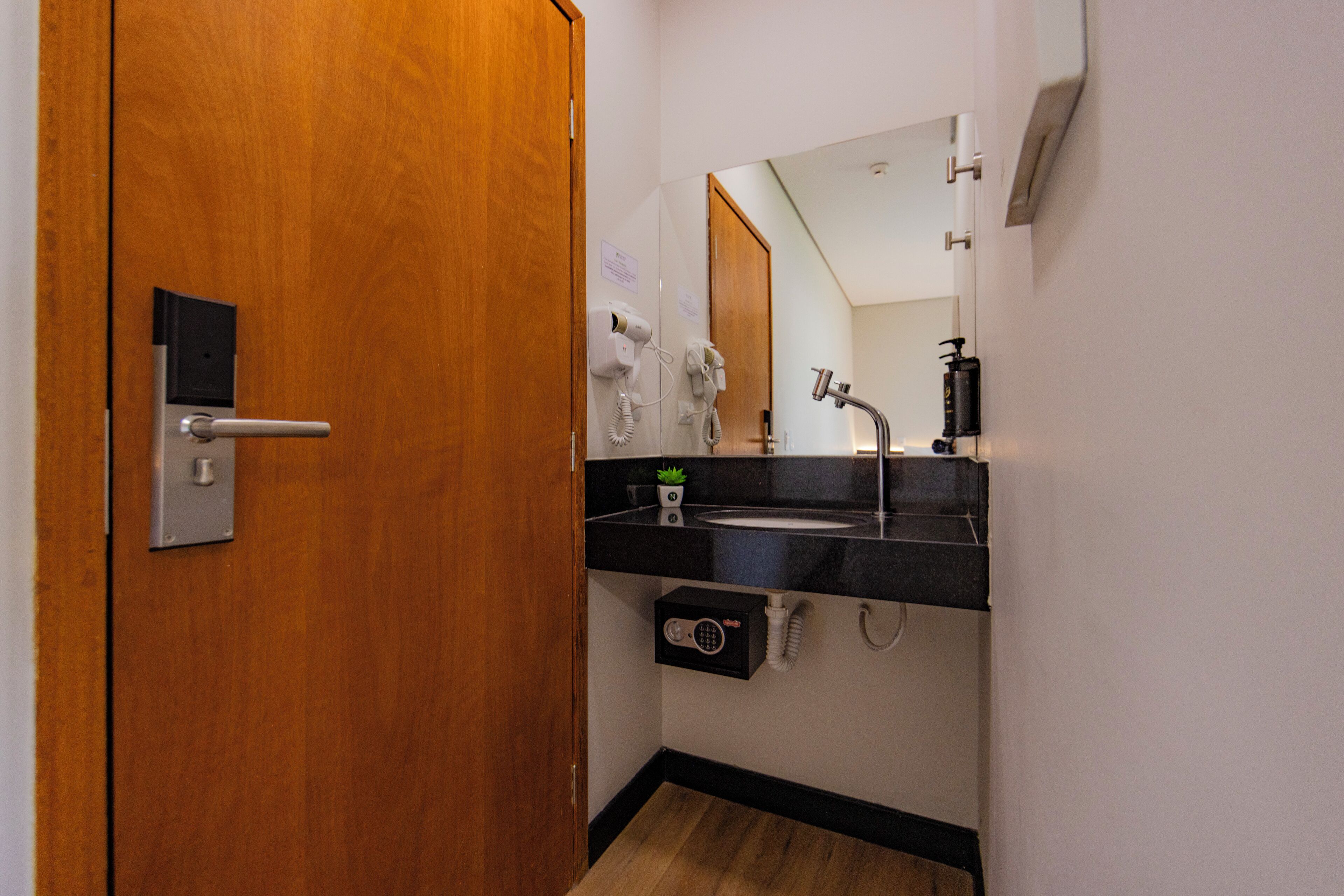 A bathroom with a wooden door, a black sink, a mirror, a hairdryer, and a towel rack.