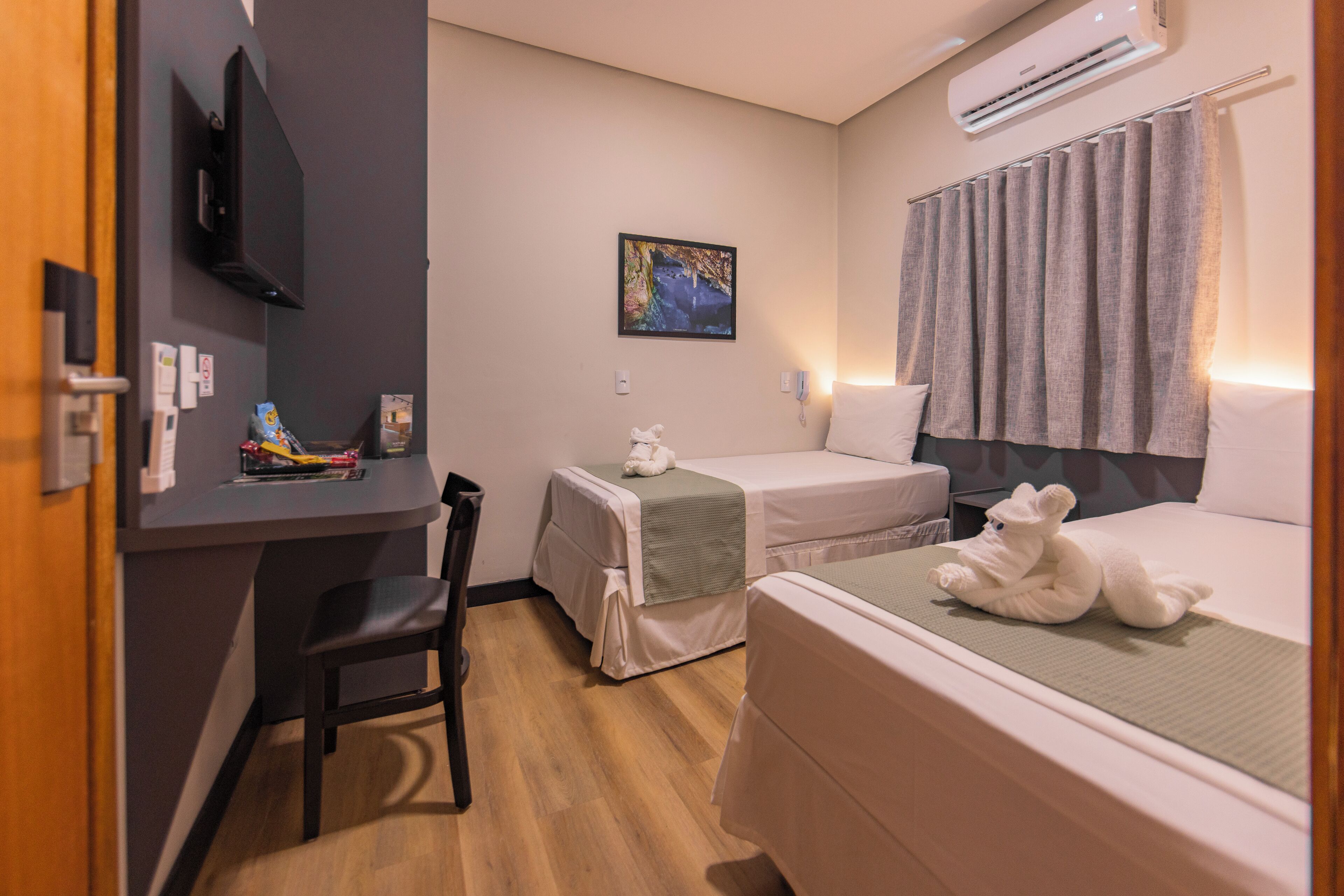 Een hotelkamer met twee bedden, een bureau, een stoel, een televisie, een airconditioner en een schilderij aan de muur.