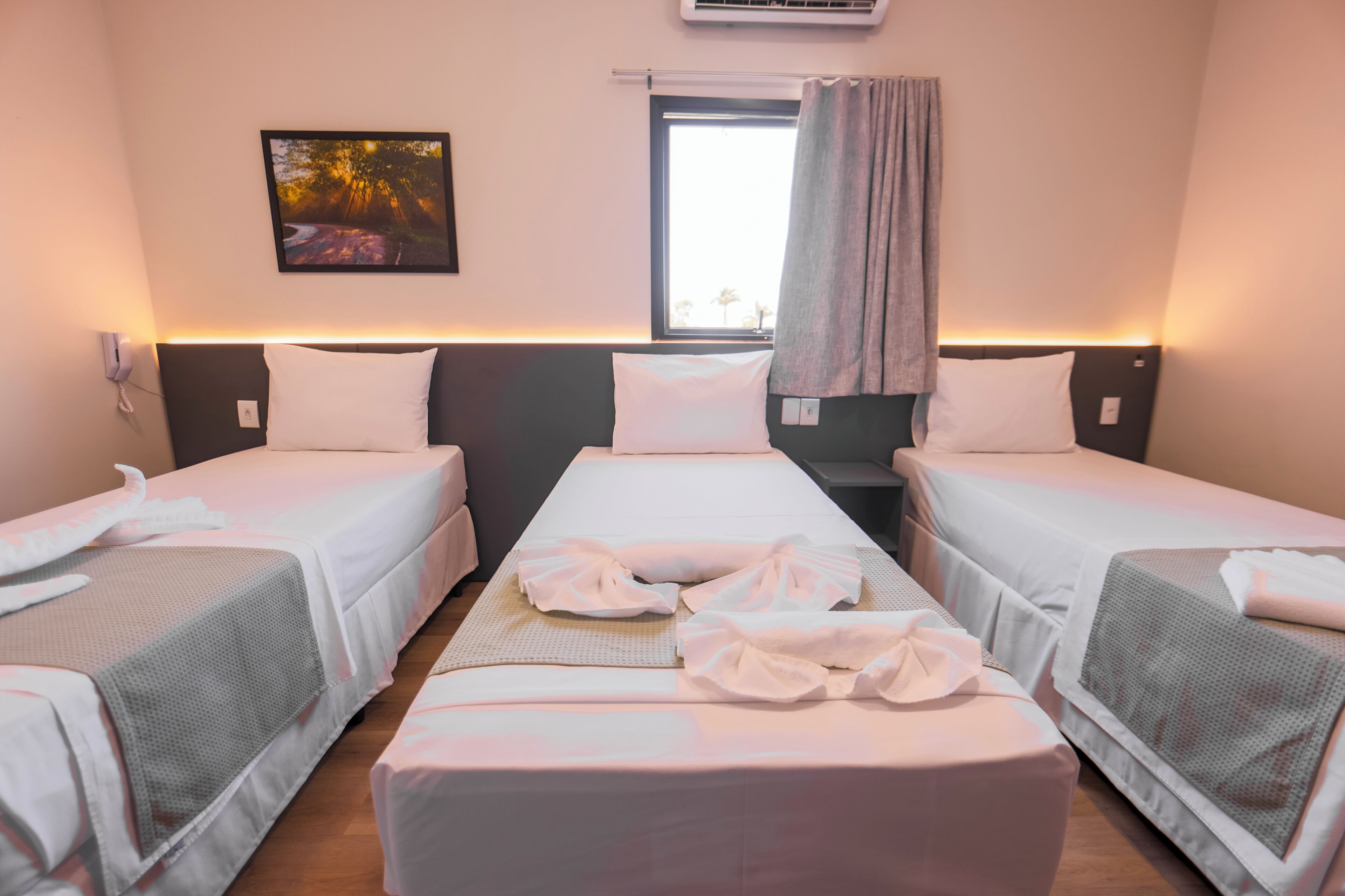 Een hotelkamer met twee eenpersoonsbedden, een groot bed, een raam met gordijnen, een airconditioning en een aan de muur bevestigde telefoon.