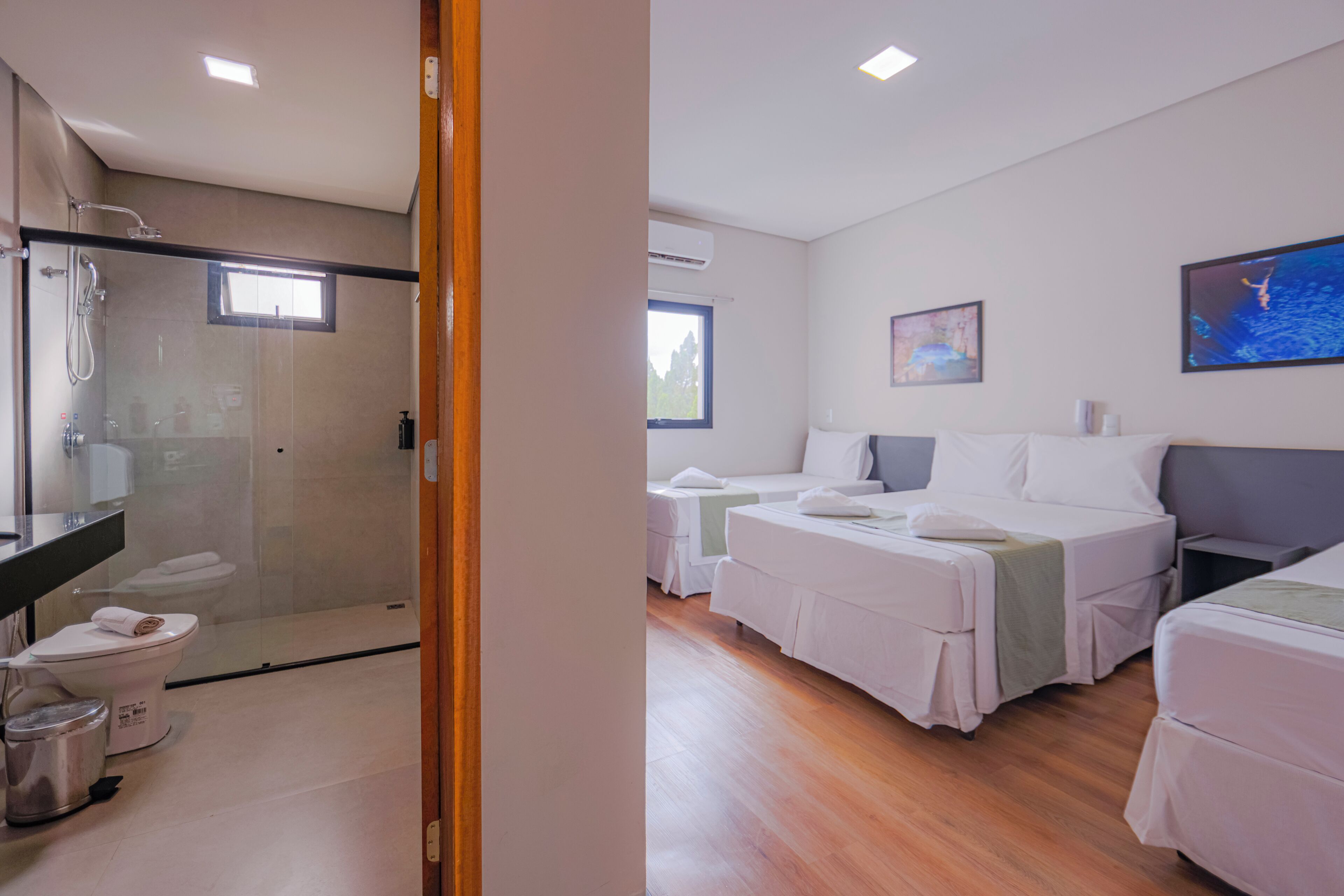 A hotel room with a glass-enclosed shower, a toilet, a bed, and a bedside table.