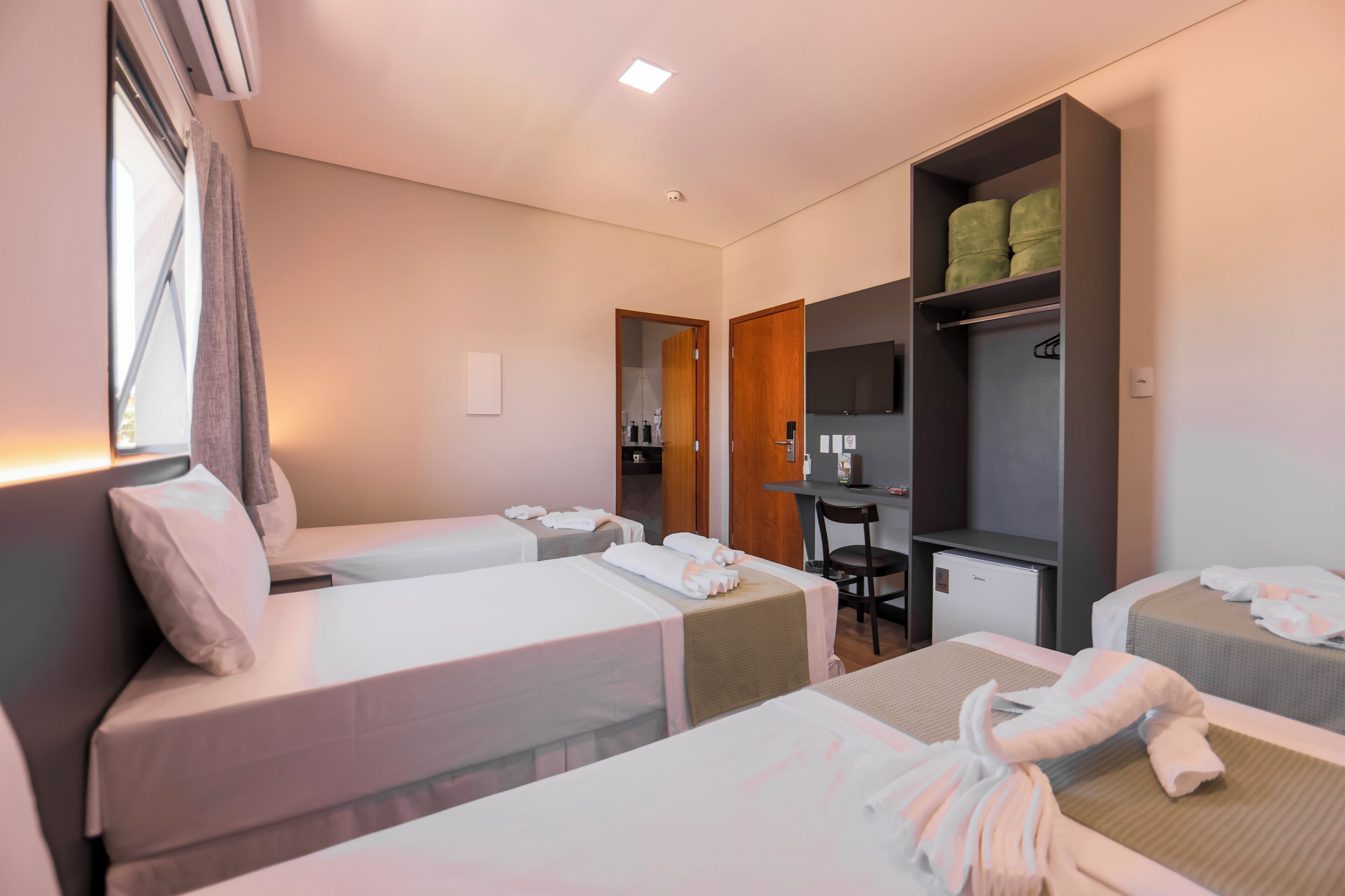 A hotel room with two beds, a desk, a chair, a TV, and a wardrobe.
