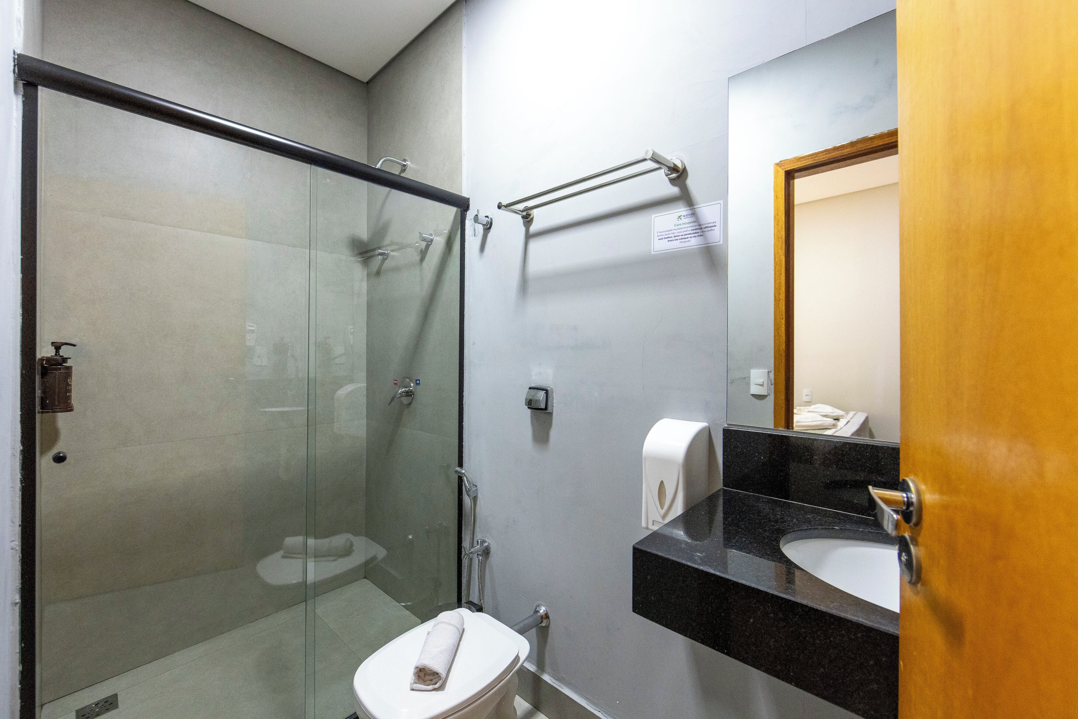 Et badeværelse med en glasafskærmet brusekabine, et hvidt toilet, en sort bordvask og en trædør.