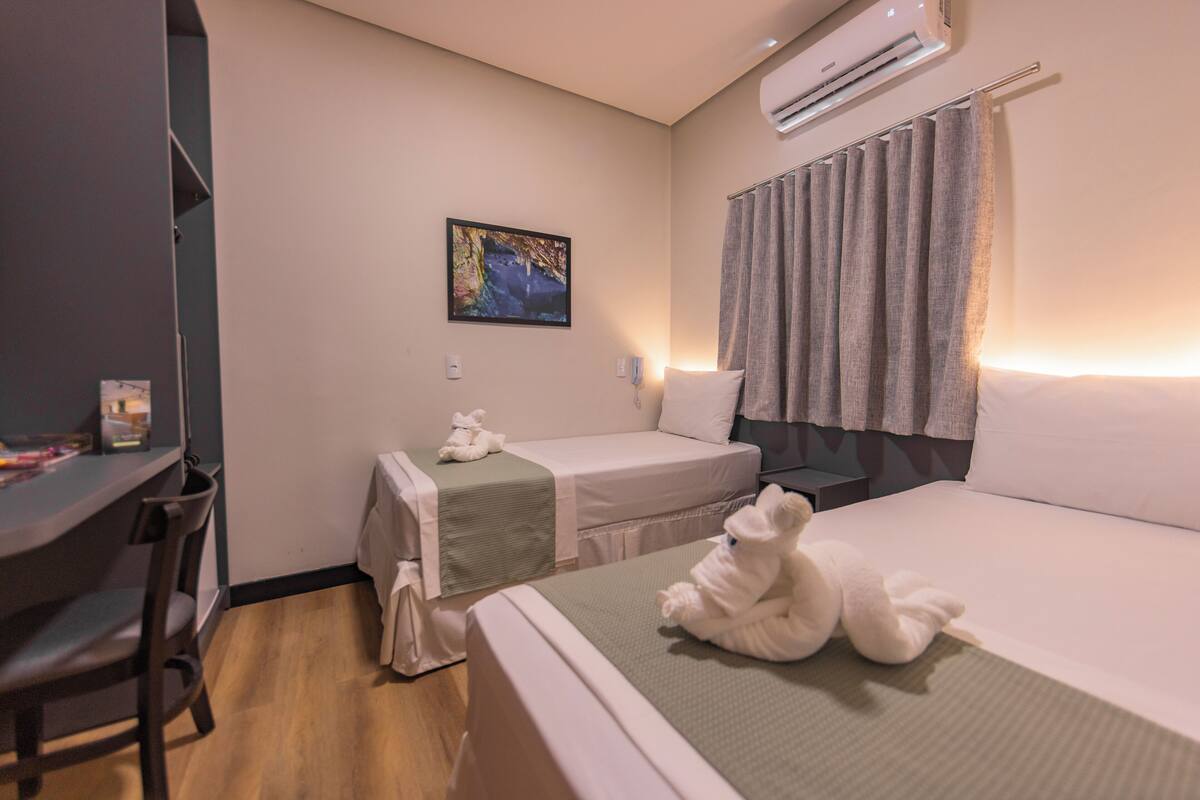 A hotel room with two beds, a desk, and an air conditioning unit.