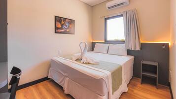 Une chambre d’hôtel avec un lit, une fenêtre avec des rideaux, un appareil de climatisation, une petite table et une chaise.
