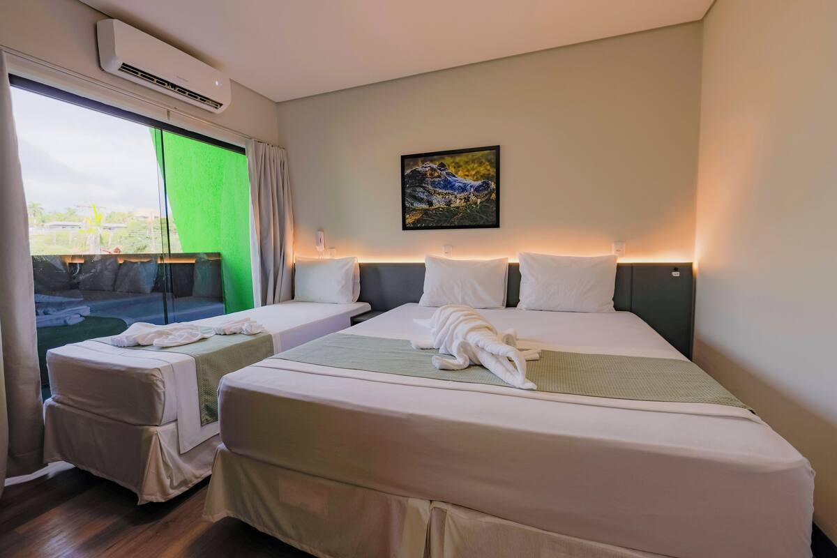 A hotel room with two beds, a large window with a view, an air conditioner, and a painting on the wall.