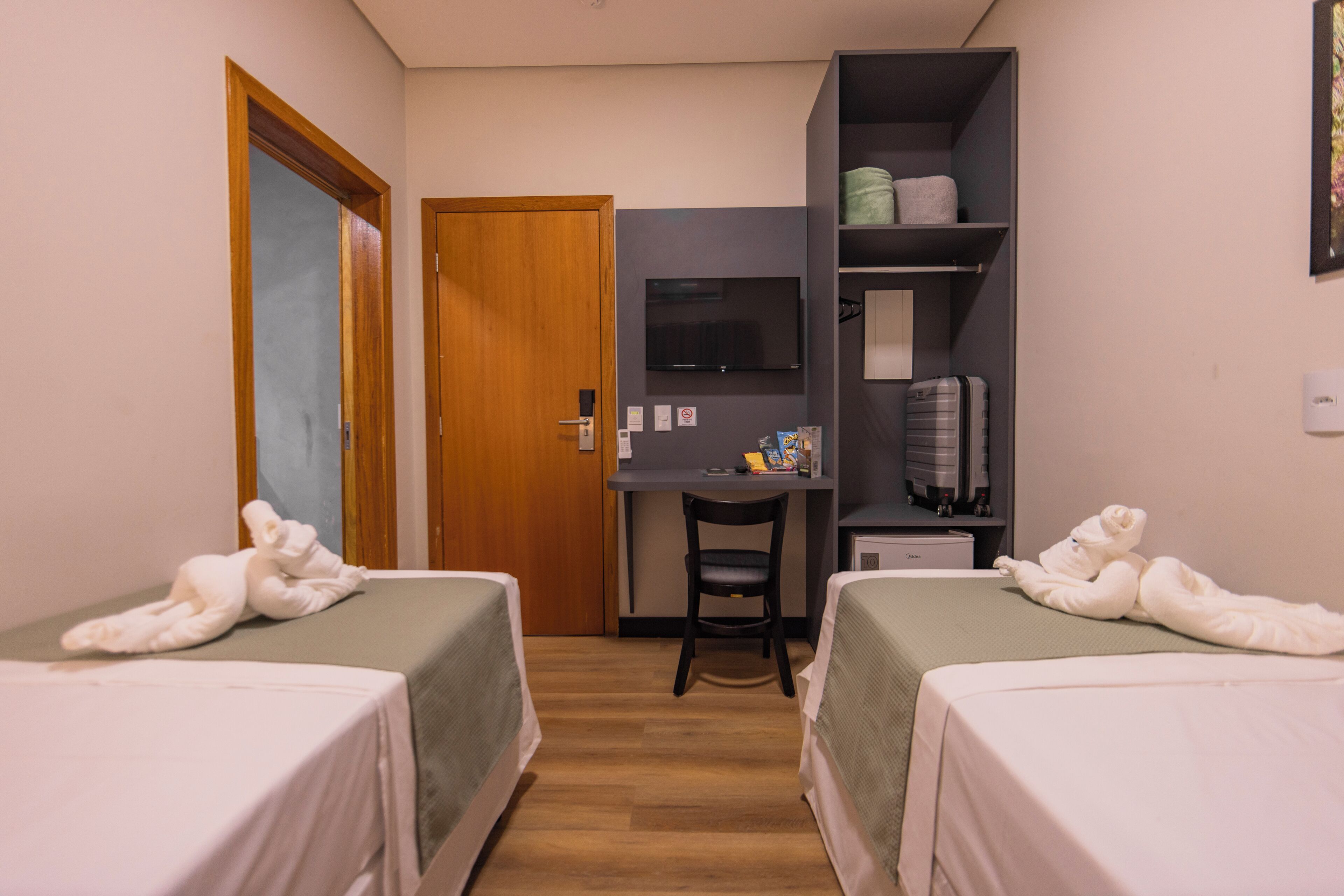 Une chambre d’hôtel avec deux lits, un bureau, une chaise, une télévision et une armoire.