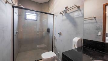 Un baño moderno con ducha de vidrio, inodoro, encimera negra y secador de manos.