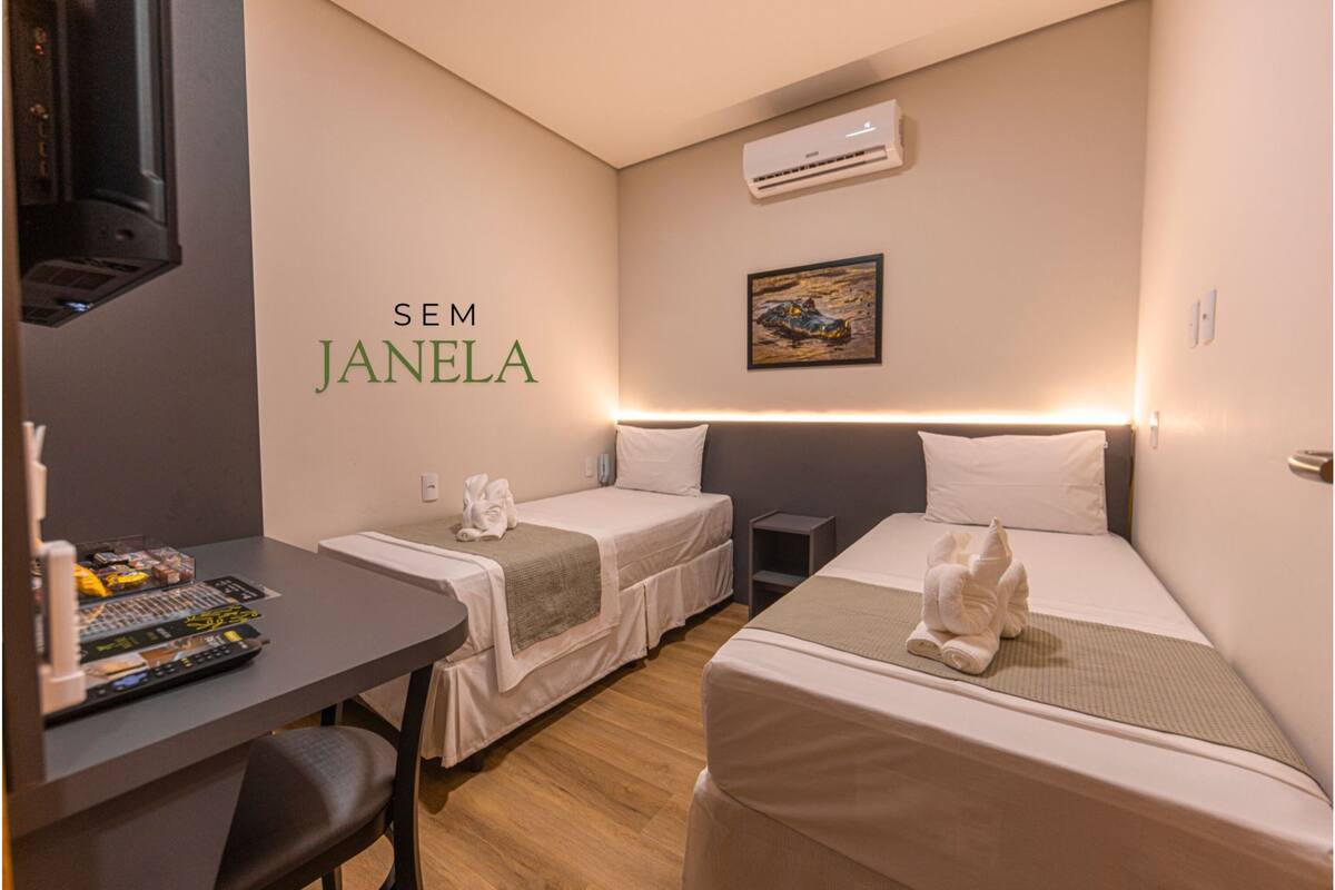 A hotel room with two beds, a desk with a TV and remote controls, and an air conditioner on the wall.