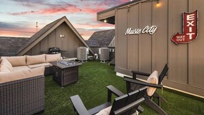Una terraza en la azotea con sofá, sillas y una mesa, un equipo de aire acondicionado, y un cartel en la pared del edificio que dice 'Exit Way Out'.