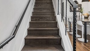 Una escalera con peldaños de madera oscura, paredes blancas y barandilla negra.