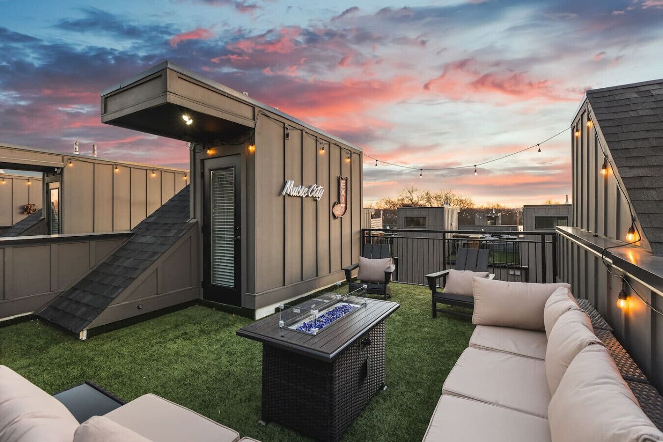 A rooftop patio with outdoor seating, a small building labeled 'Music City', and a sunset sky.