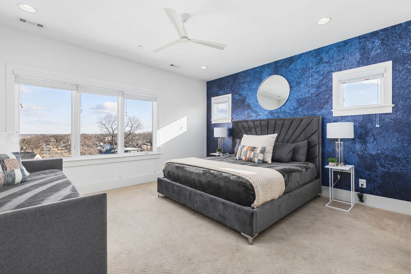 A modern bedroom with a large bed, a ceiling fan, and a view of the outside.