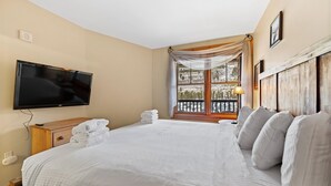 Una habitación de hotel con una cama grande, un televisor de pantalla plana, un ventanal con vistas a un paisaje nevado y un cabecero de madera.