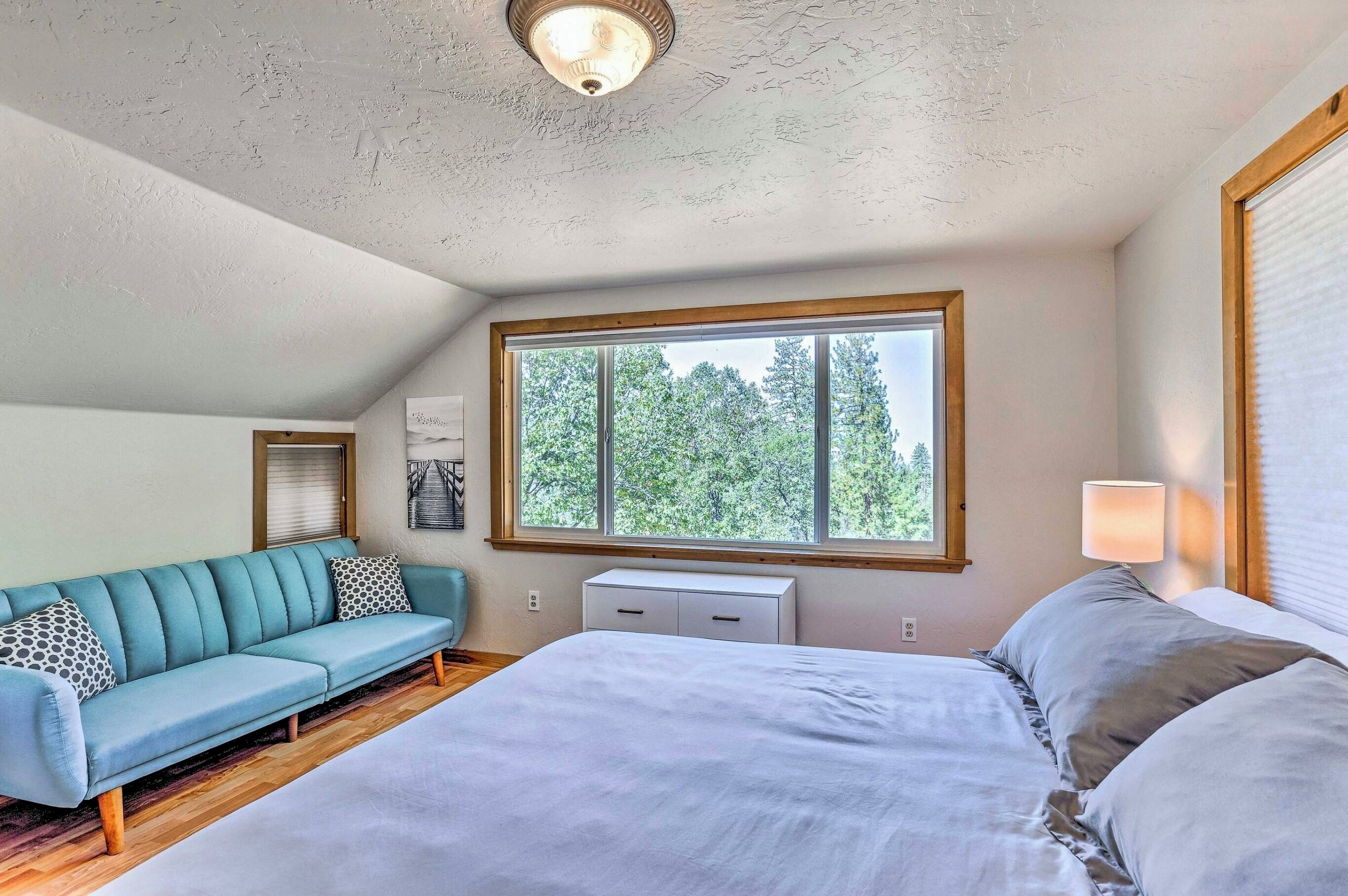 Una camera da letto con un letto, un divano, una finestra vista alberi e una luce a soffitto.