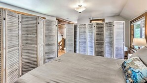 Un dormitorio con una cama grande, contraventanas de madera en las paredes, un ventilador de techo y una ventana con vistas.