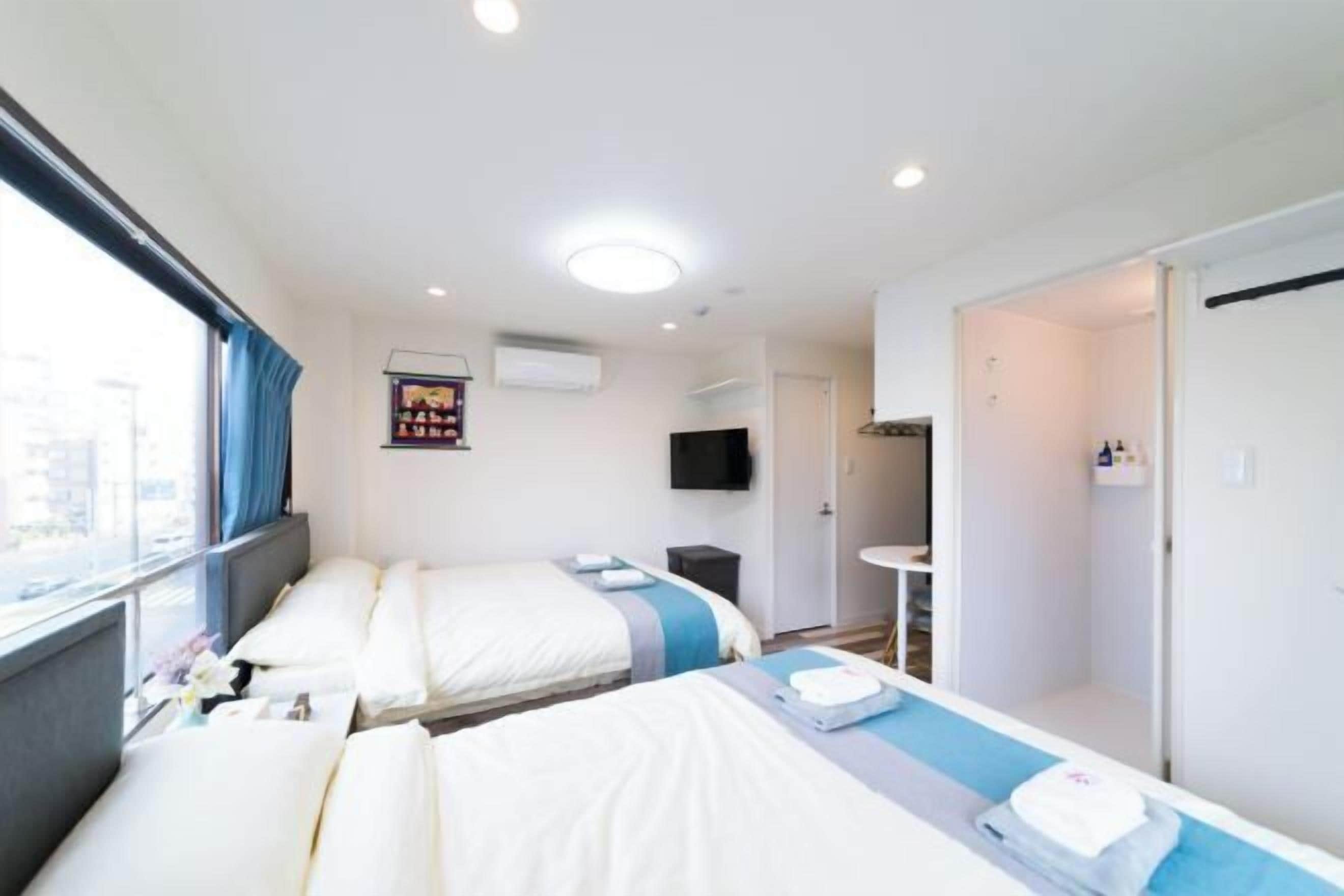 Une chambre d’hôtel avec deux lits, une télévision, une petite table et une fenêtre avec des rideaux.