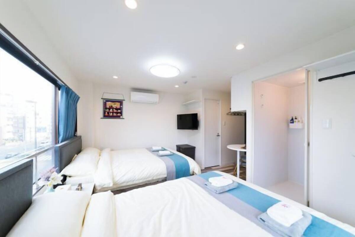 A hotel room with two beds, a TV, a small table, and a window with curtains.