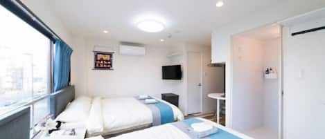 A hotel room with two beds, a TV, a small table, and a window with curtains.