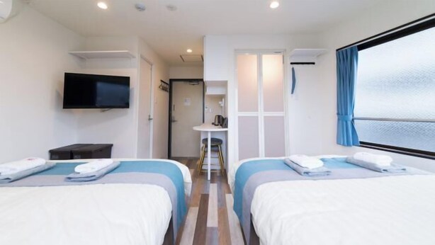Ett hotellrum med två sängar, en tv, ett litet bord och ett fönster med gardiner.