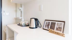 Ett rent, vitt kök med en vattenkokare, ett inramat foto och en skylt med texten ”Välkommen”.