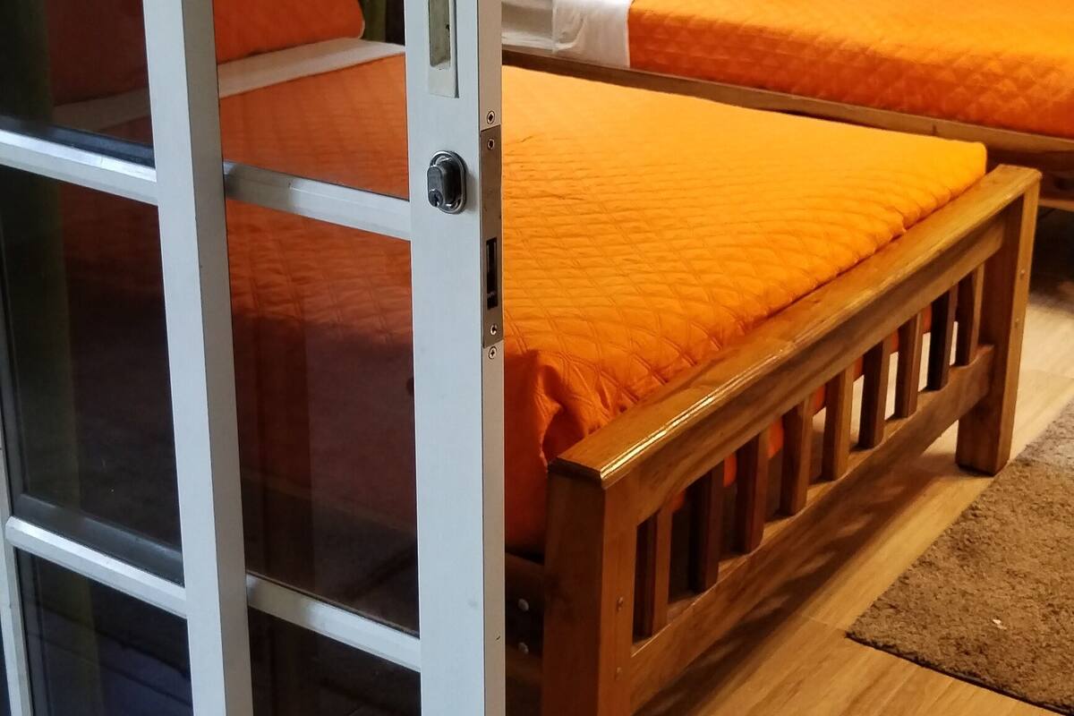 Ein Zimmer mit zwei Betten, einer Schiebetür aus Glas und einer kleinen Klimaanlage an der Wand.