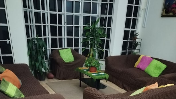 Een woonkamer met bruine banken, een salontafel en grote groene planten.