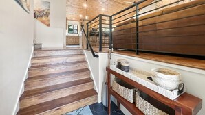 A wooden staircase with a metal railing, leading to a kitchen area with wooden cabinets and a stone wall. - Family-Friendly 5BR | Gather, Relax & Explore (Park City)