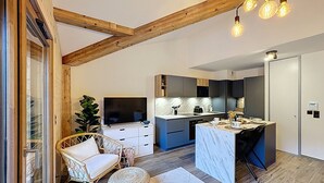 A modern kitchen with a marble countertop, wooden ceiling beams, and a dining area with a wicker chair and ottoman. - Tauari - Les Gets - Les Perrières (Les Gets)