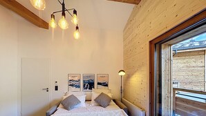 A bedroom with a wooden ceiling, a bed with white bedding and towels, a bedside lamp, and a view of a wooden deck through a large window. - Tauari - Les Gets - Les Perrières (Les Gets)