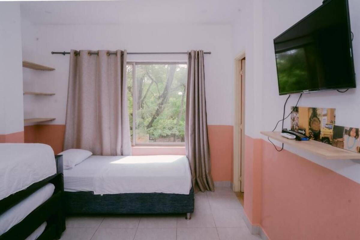 A bedroom with two beds, a TV, a window with curtains, and a shelf with items.