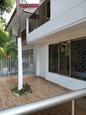 Un edificio moderno de dos pisos con amplios ventanales, una terraza de madera y una valla metálica.