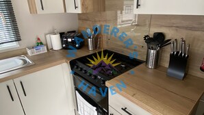 A modern kitchen with white cabinets, a black stove, and wooden countertops. - Wanderer's Haven - Dog-Friendly Static Caravan near Cockermouth (Cockermouth)