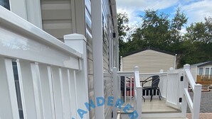 A deck with a white railing, a small wooden bench, and a patio area with a table and chairs. - Wanderer's Haven - Dog-Friendly Static Caravan near Cockermouth (Cockermouth)