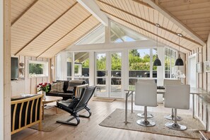 Una habitación amplia con techo alto, ventanas grandes, comedor y zona de estar con sofá y sillones.
