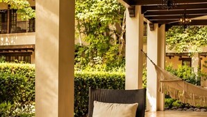 Un patio al aire libre con mobiliario de mimbre, una hamaca colgante y una planta en maceta.