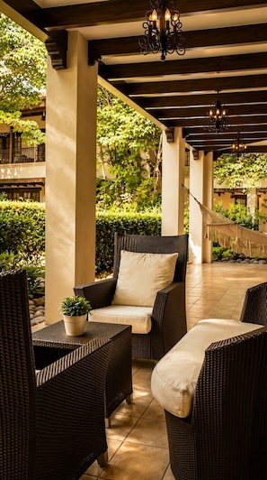 Un patio al aire libre con mobiliario de mimbre, una hamaca colgante y una planta en maceta.