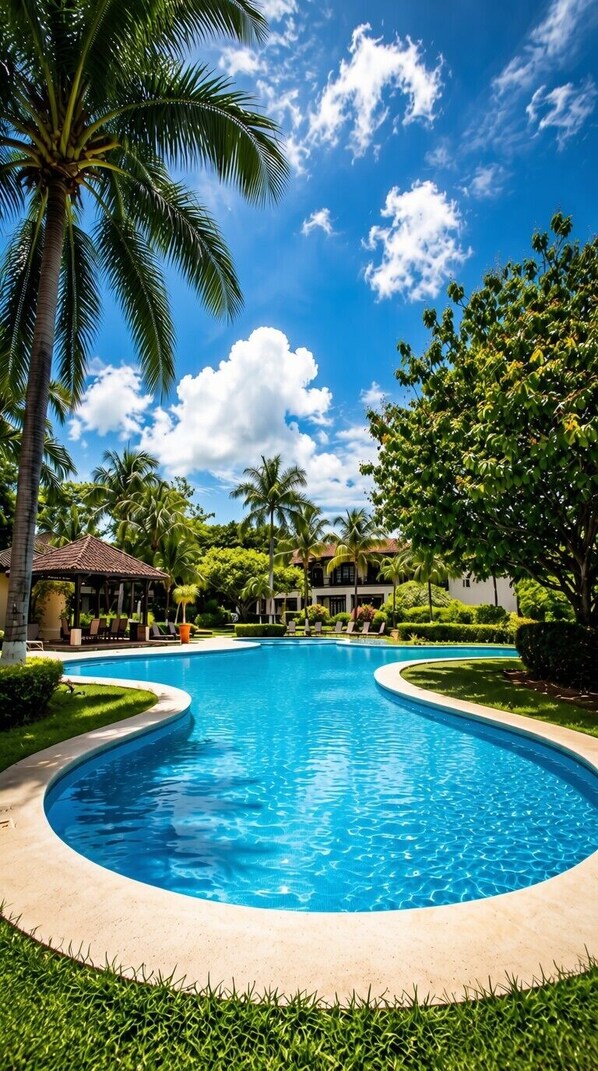 Une piscine à bordures courbes, entourée de palmiers et de verdure, sous un ciel bleu dégagé.