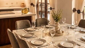 Un comedor con una mesa dispuesta para seis personas, rodeada de sillas, y una cocina al fondo.