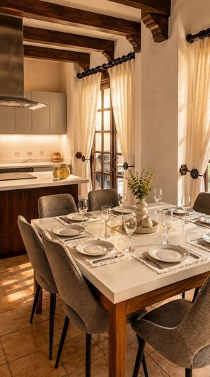 Un comedor con una mesa dispuesta para seis personas, rodeada de sillas, y una cocina al fondo.