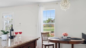 Una cocina con encimera de granito, una mesa de comedor con individuales negros, una araña y vistas de un jardín a través de una ventana.