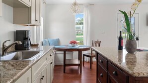 Una cocina moderna con encimera de granito, pileta de acero inoxidable y cafetera. Hay una mesa de comedor con sillas y un florero.