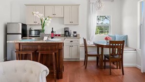 Una cocina moderna con armarios blancos, una zona de comedor con sillas de madera y un amplio ventanal con vistas a zonas verdes.