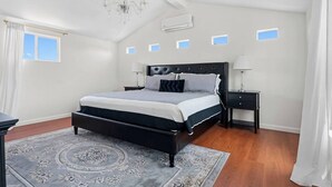 A bedroom with a large bed, two bedside tables, a chandelier, and a window with curtains.
