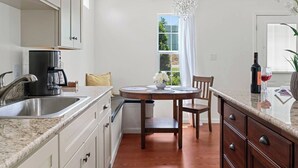 A modern kitchen with a coffee maker, a dining table with chairs, and a view of the outdoors through a window.