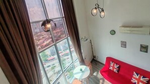 A room with a large window, a red sofa, a small round table, and a hanging light fixture. - The CEO By SY Staycation (Bayan Lepas)